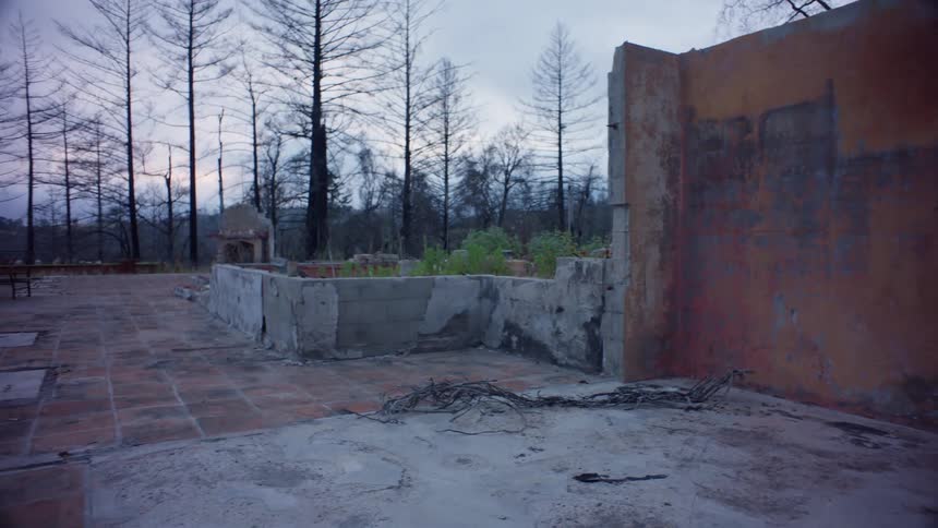 A woman works on a pottery wheel outdoors surrounded by trees and worn and weathered walls
