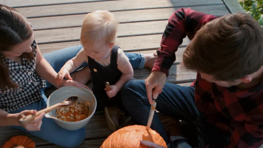 A family carving a jack o lantern on the porch at dusk