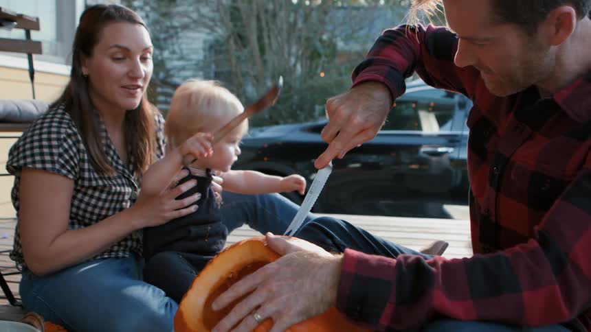 Father with a knife cutting a pumpkin while mother and young son next to him watch having fun