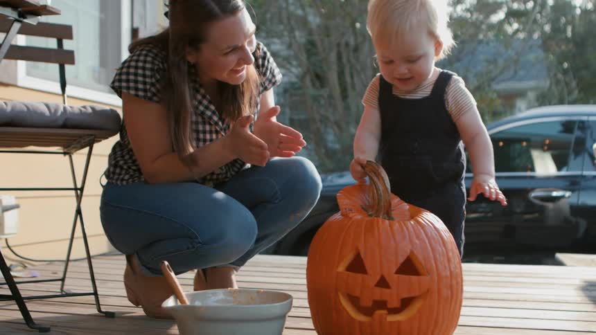 Little boy next to his mother playing with a halloween pumpkin