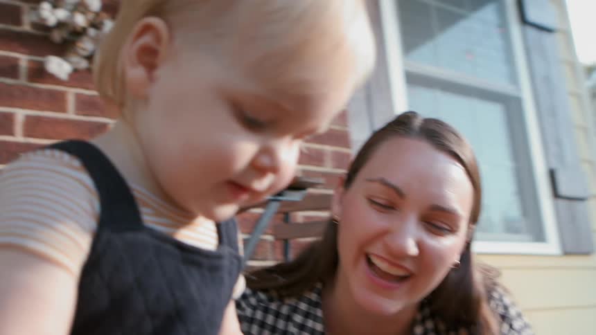 A mother and father help their toddler son carve a pumpkin while sitting outdoors