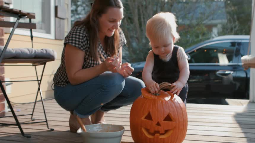 Mother and son playing with a jack o lantern on the porch at dusk