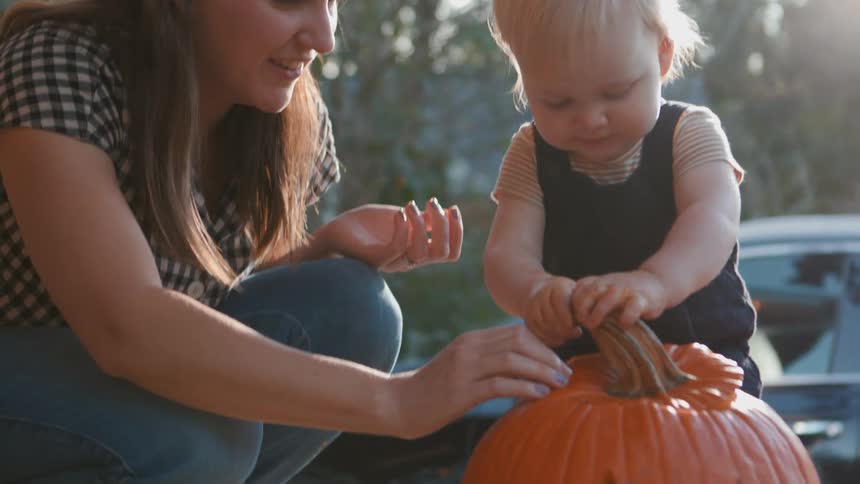 Mother helps her child put the top back onto a carved jack o lantern near their home