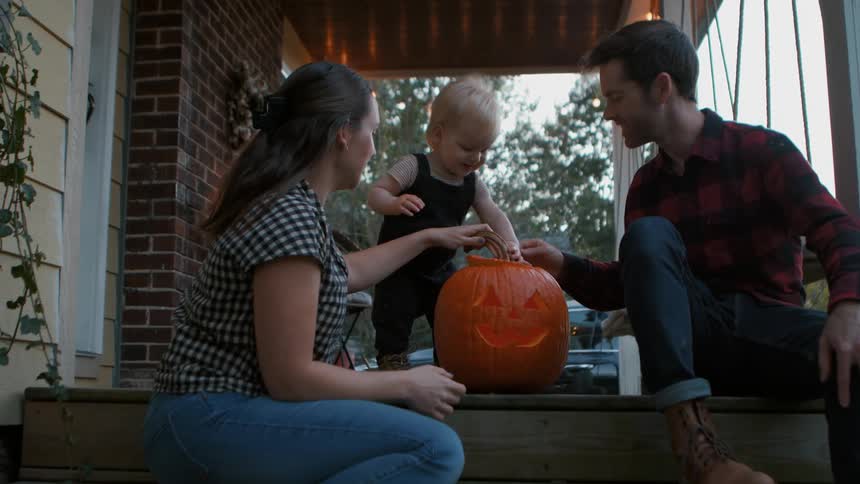 A family carving a jack o lantern on the porch at dusk