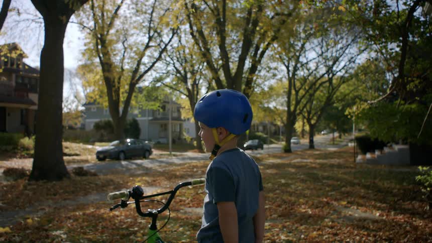 Young bicycle rider straddles a bike in a front yard strewn with fallen leaves
