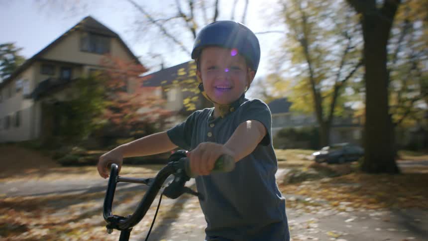 A happy child rides a green bicycle in the neighborhood reaching for the camera