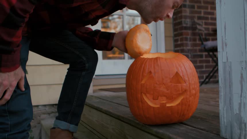Man blows out the flame in a jack o lantern before climbing the porch steps