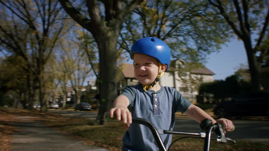 A child wearing a helmet rides a bicycle in the neighborhood during fall