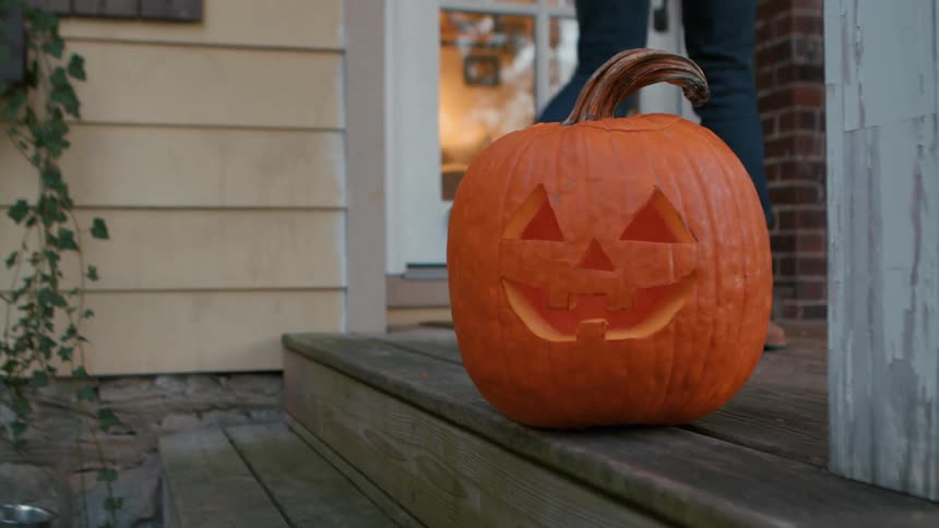 A person leaves a carved jackolantern on a porch lit from within