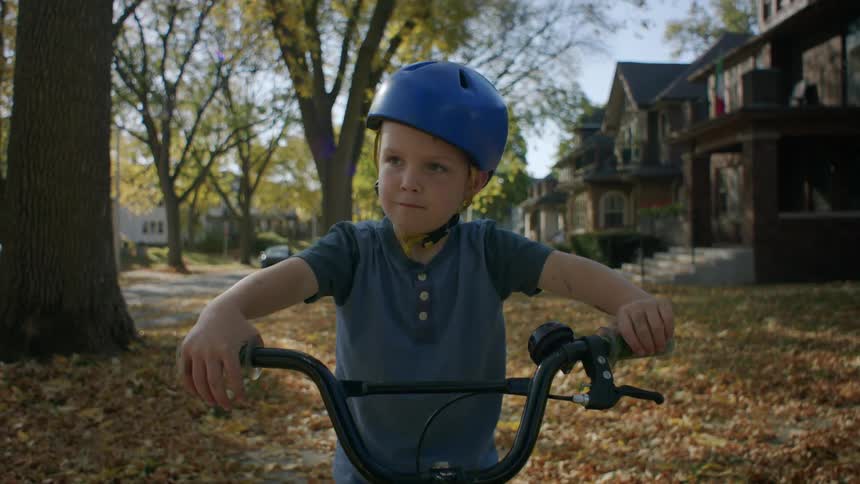 A child wearing a helmet rides a bicycle in the neighborhood during fall
