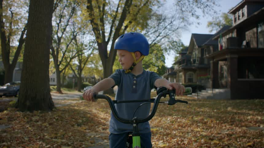 A child wearing a helmet rides a bicycle in the neighborhood during fall