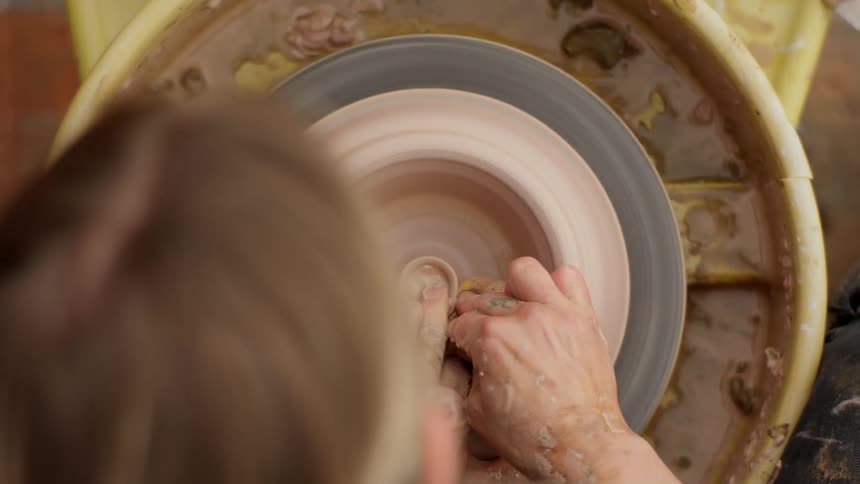 Overhead of a woman molding clay on a pottery wheel