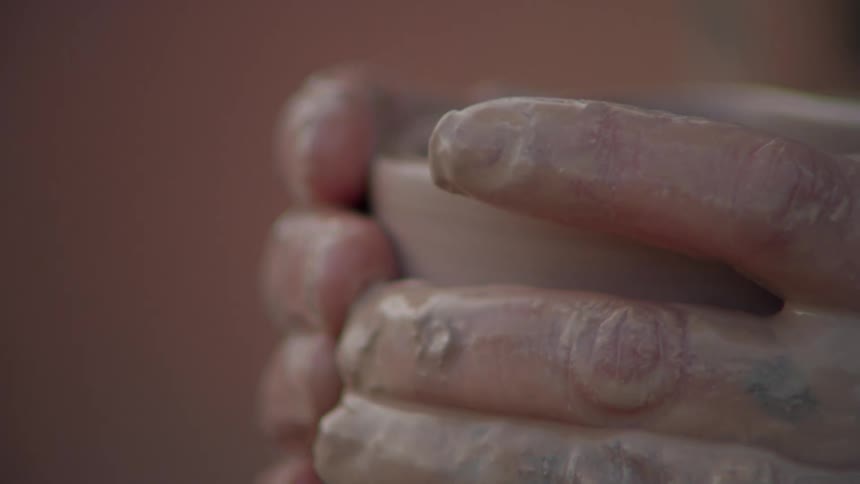 Close up of a persons hands molding a clay vase