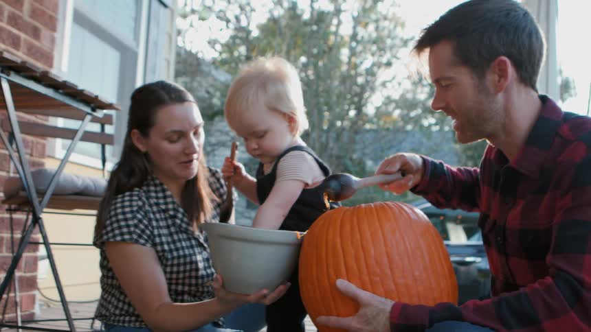 A family carving a jack o lantern on the porch at dusk