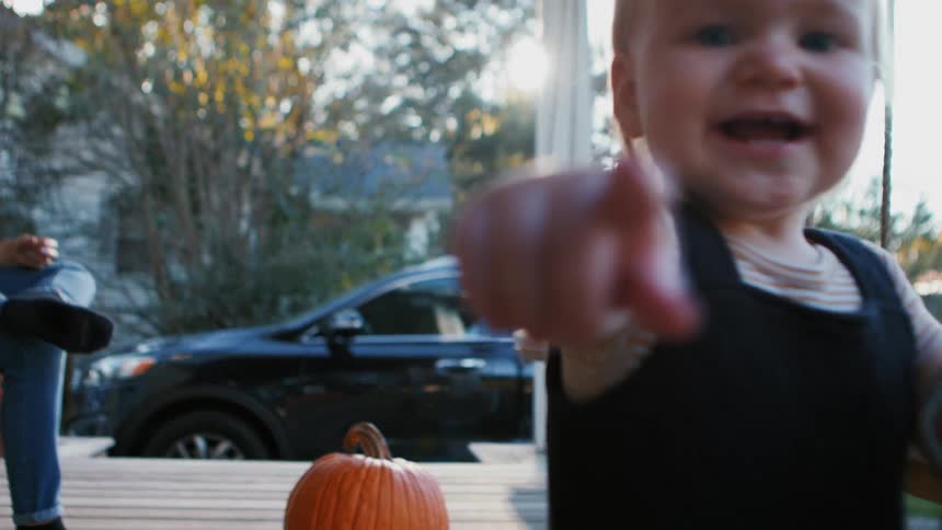 A toddler holding a watering can outside walks forward and points while smiling