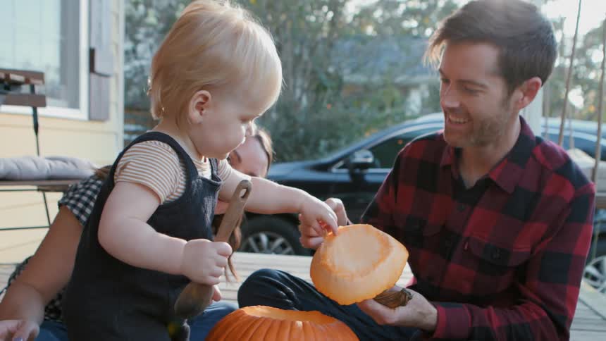Little boy touching a pumpkin next to his parents