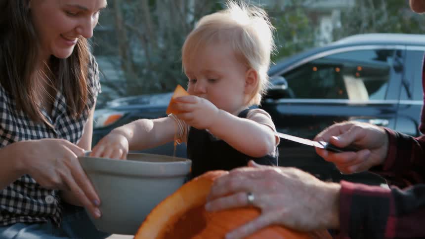 Two parents have fun helping their toddler carve up a pumpkin