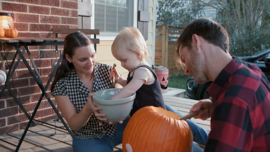 A family carving a jack o lantern on the porch at dusk