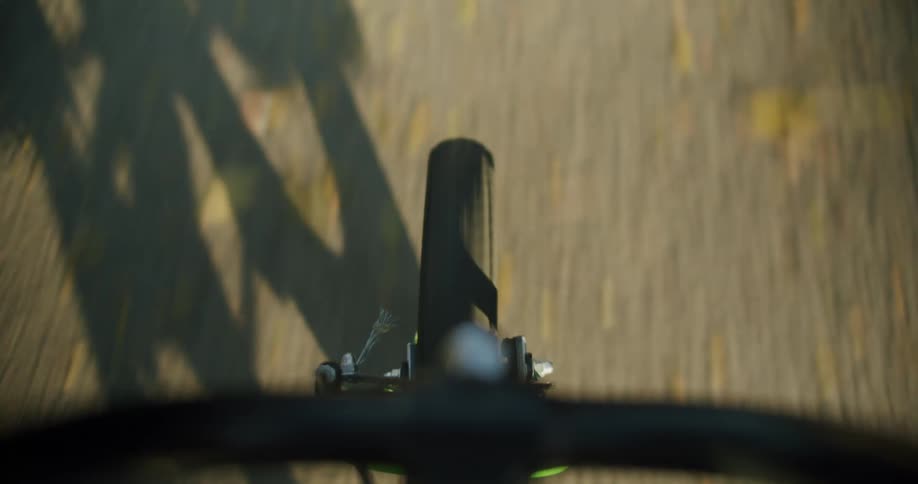 A bicycle tire rolls along a paved road casting a shadow on the ground