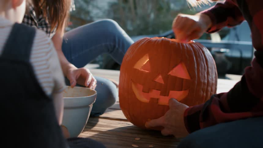 A family carves a jackolantern on the porch