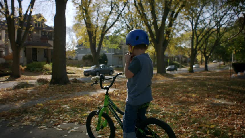 A child wearing a helmet rides a bicycle in the neighborhood during fall