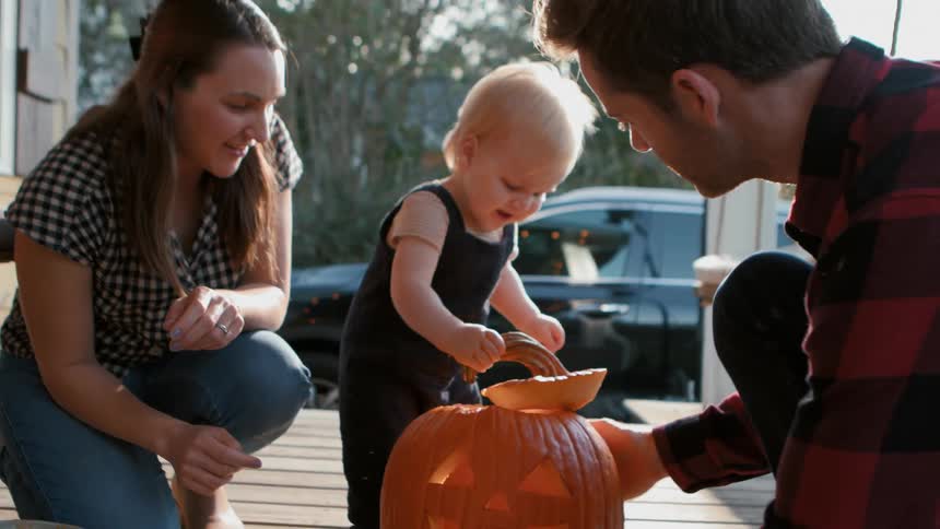 A family playing with a jack o lantern on the porch at dusk