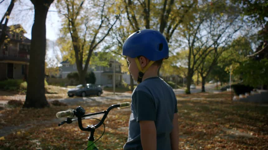 A boy sits on a bicycle wearing a helmet in a yard in a suburb