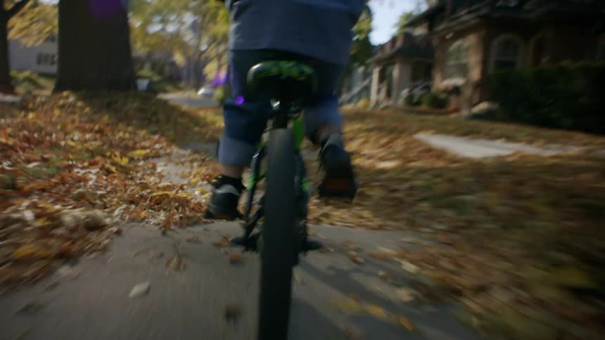 A child wearing a helmet rides a bicycle in the neighborhood during fall