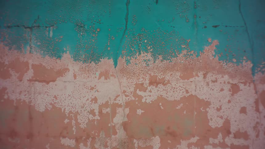 Closeup of a weathered textured wall with chipping paint in shades of blue