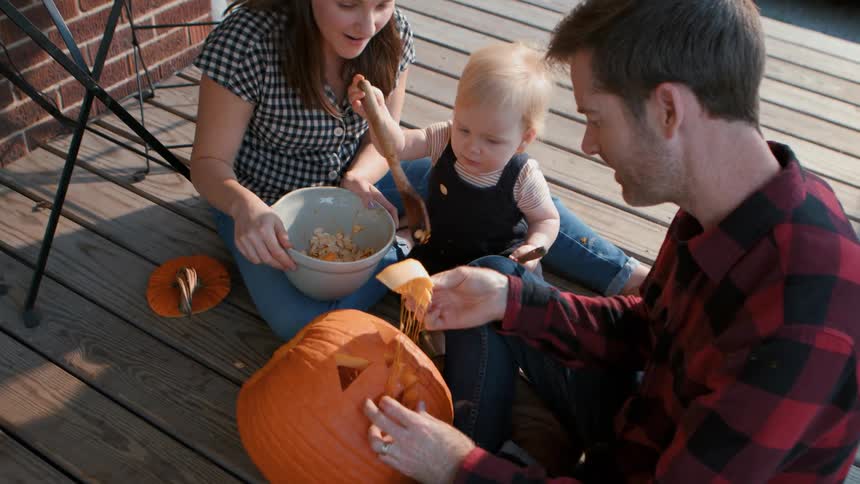 Father and mother with their little daughter preparing a halloween pumpkin