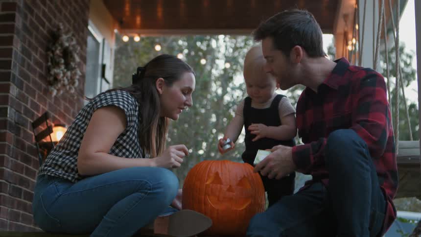 Little boy placing a candle inside a halloween pumpkin next to his parents