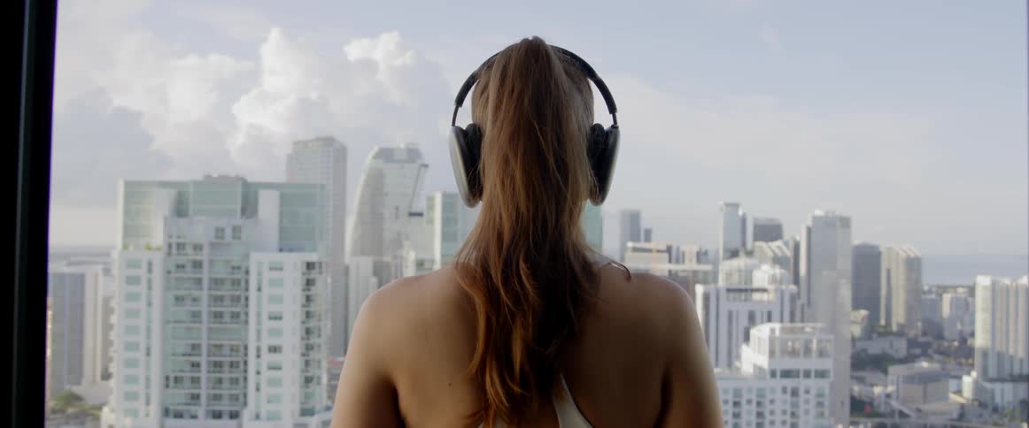 View of a woman from behind putting on headphones while looking at a view of a metropolis with skyscrapers