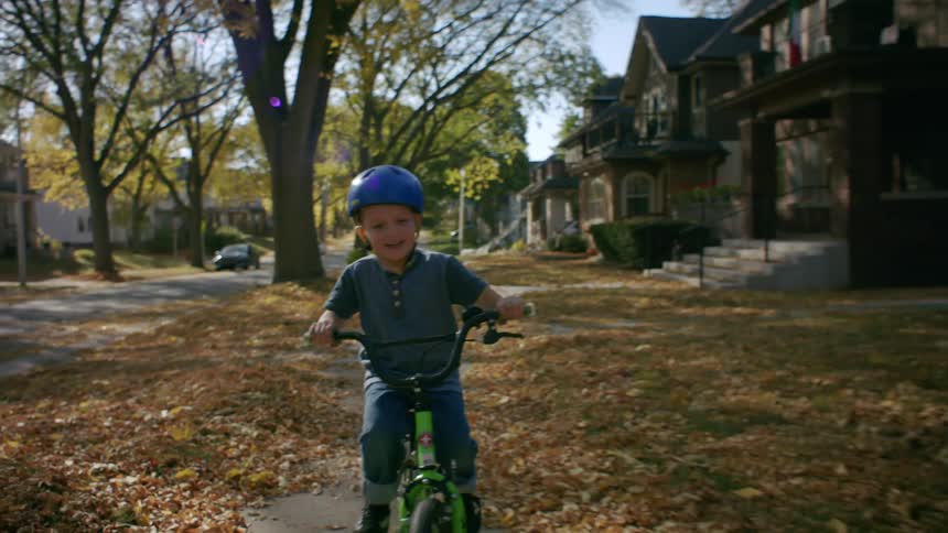 A child wearing a helmet rides a bicycle in the neighborhood during fall