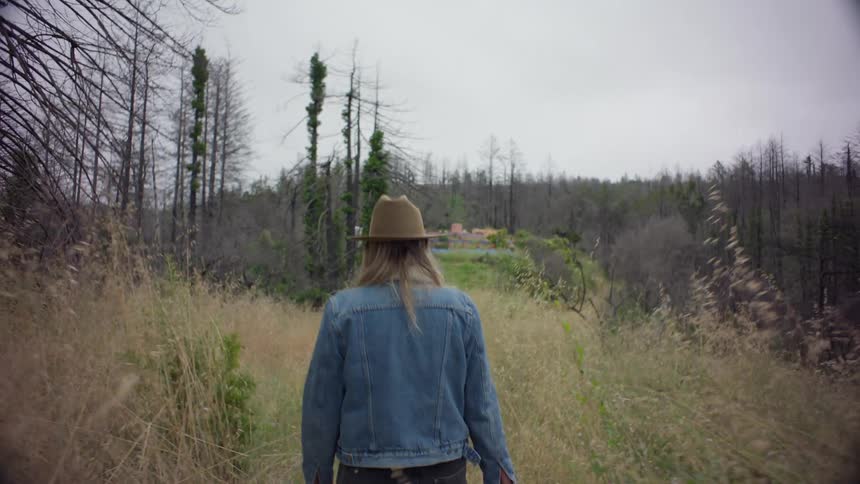 Woman carrying a shovel and bucket through an overgrown path in the forest