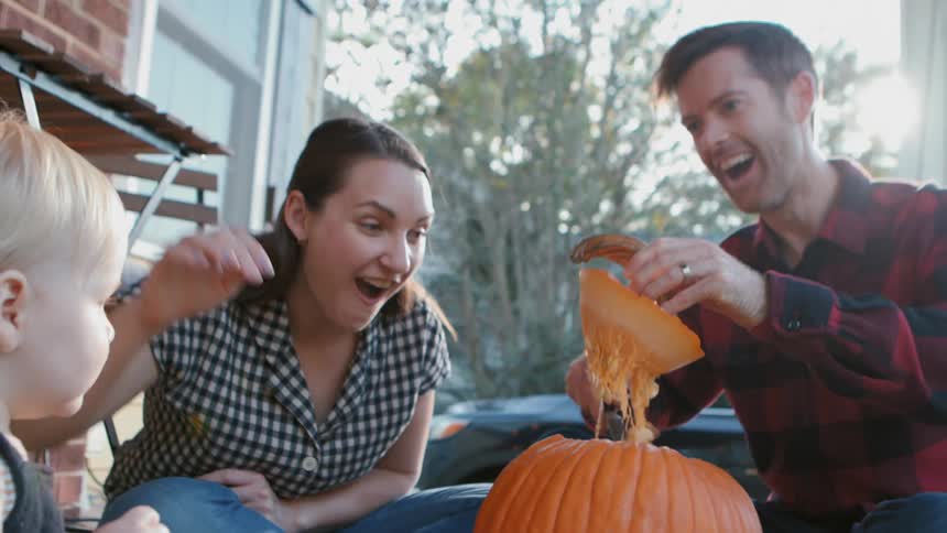 A family carving a jack o lantern on the porch at dusk