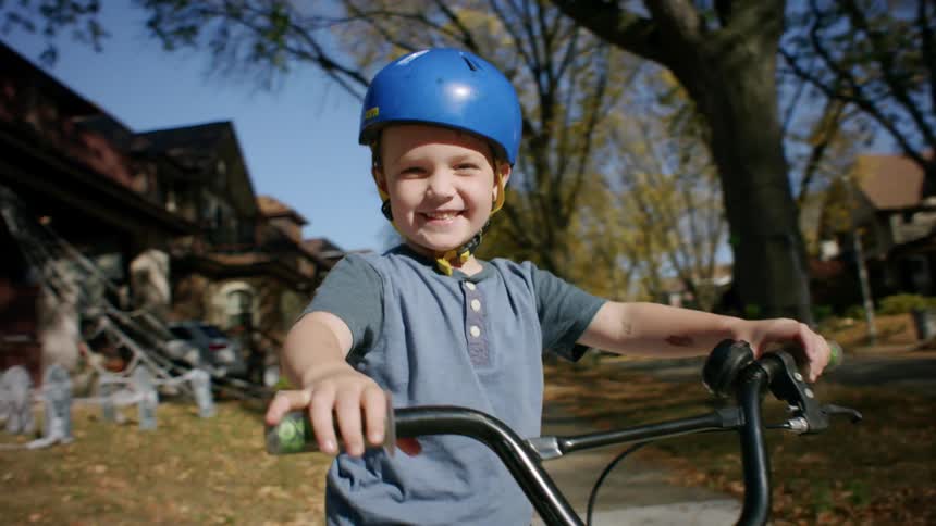 A child wearing a helmet rides a bicycle in the neighborhood during fall