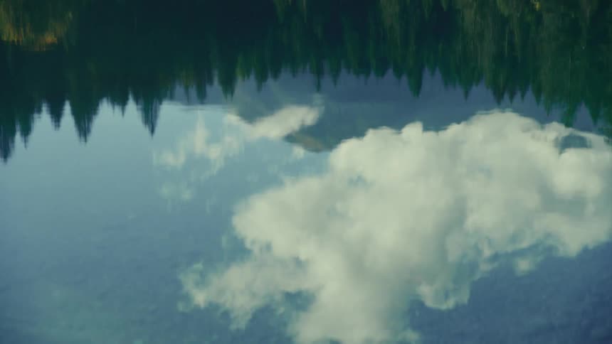 Lake reflecting the sky with clouds and the silhouette of conifers around