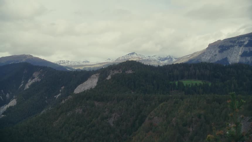 Aerial view of mountains covered in dense evergreen forest with snowcapped peaks in the background
