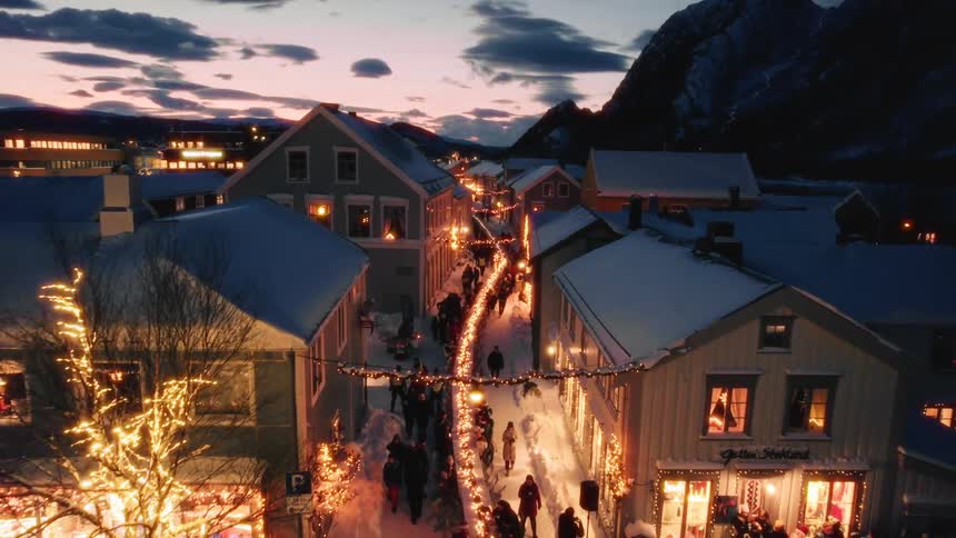 A small town is illuminated with christmas lights with people walking through the streets