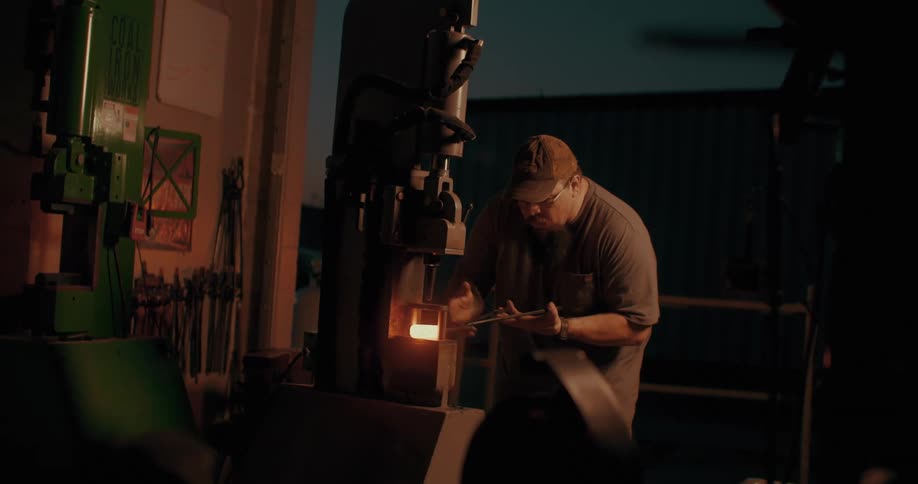 Man with tweezers picking up heated metal and placing it in a machine carefully