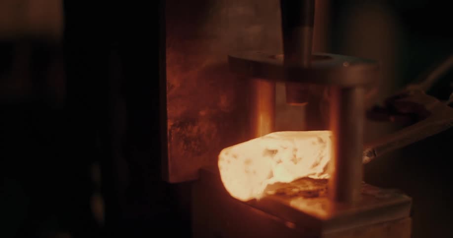 Closeup of a heated piece of metal being forged by a machine