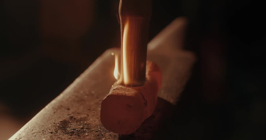 Wooden handle being placed on a forged hammer from which fire begins to come out a little