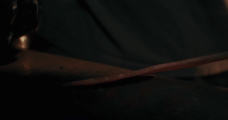 A blacksmith uses a hammer to shape a piece of metal over an anvil