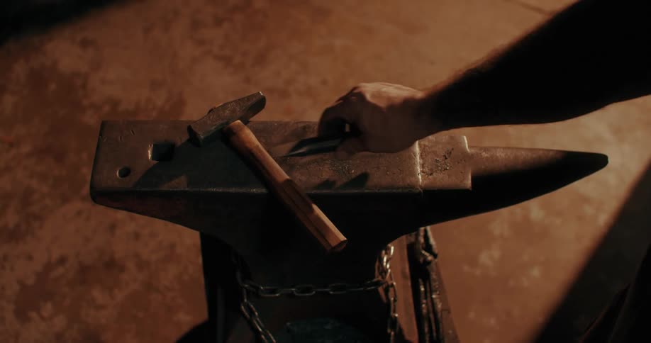 A blacksmith puts down his tool on the anvil