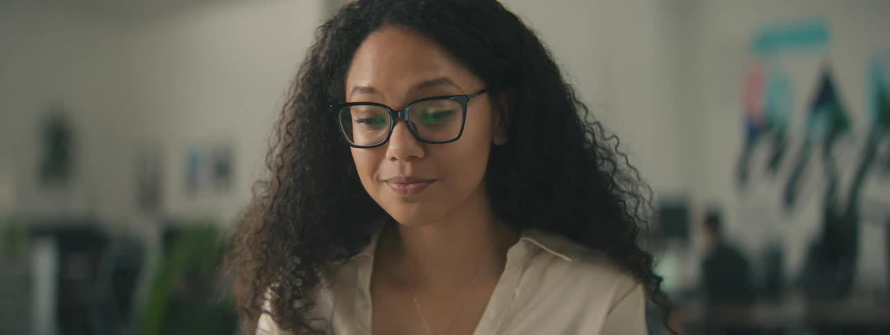 A happy woman with curly hair takes a video call on a laptop in the office