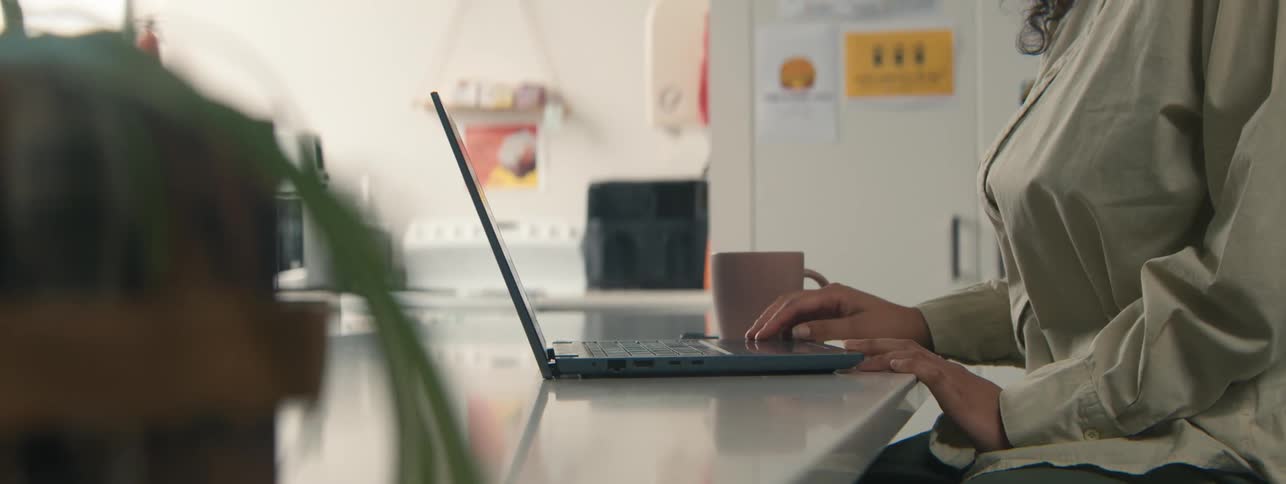 A woman opens her laptop and drinks tea