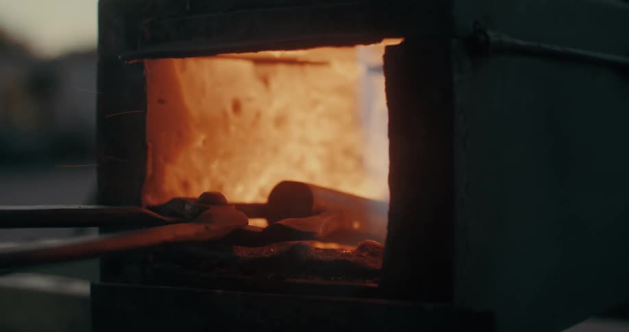 A blacksmith heating a piece of metal on a small outdoors furnace