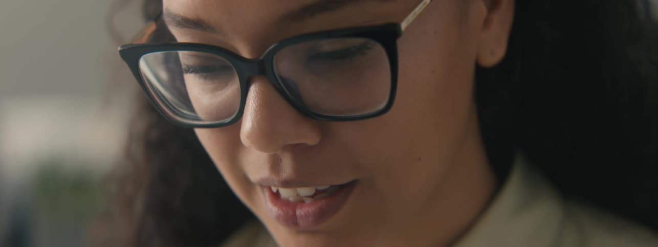 Closeup of the face of a young woman with curly hair and glasses focused on a task