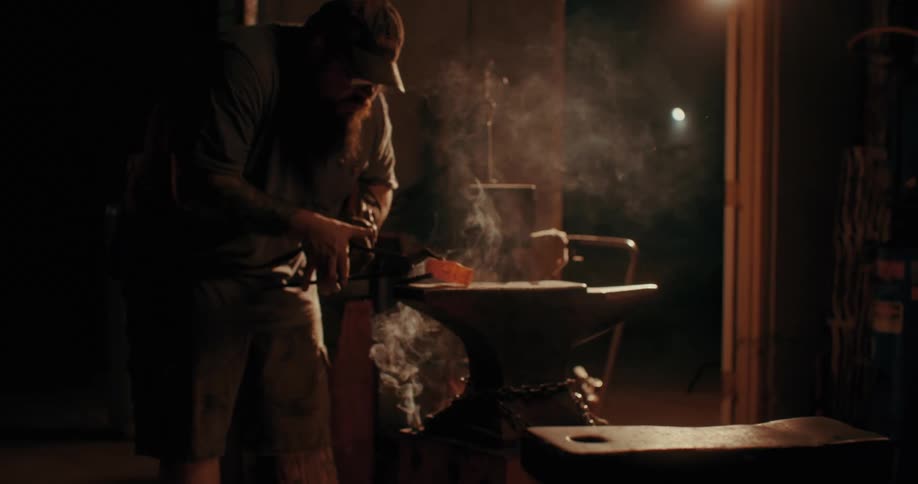 A blacksmith placing a hot piece of metal over an anvil in a dimly lit workshop