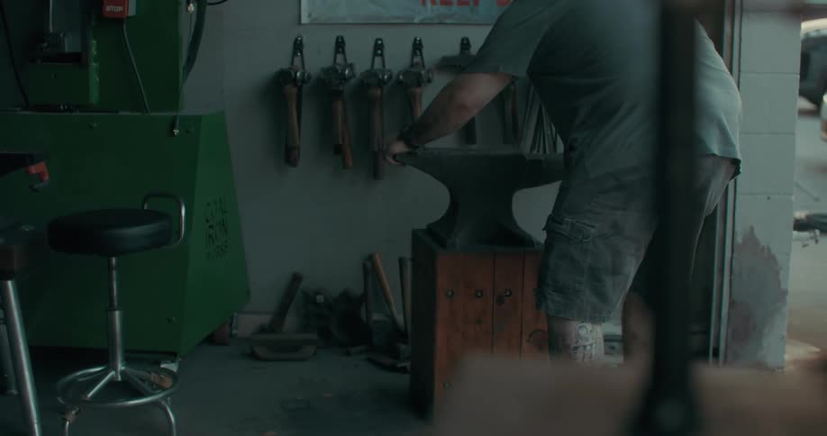 A blacksmith pulls an anvil out of the workshop at morning